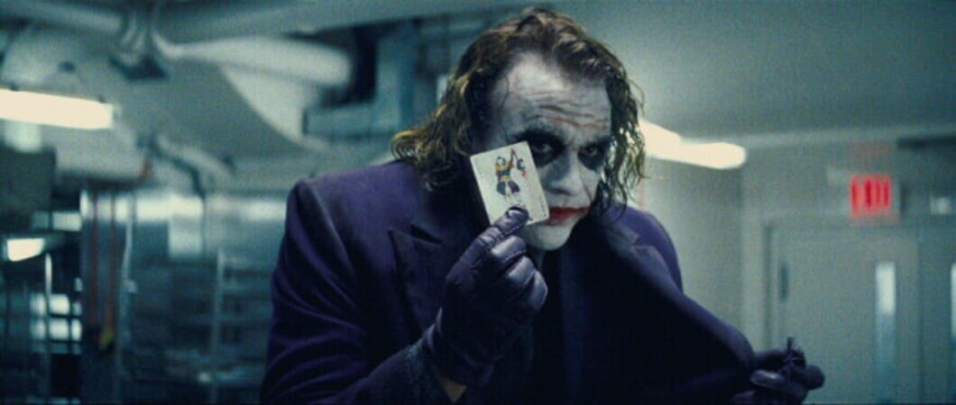 The Joker holds up a Joker playing card. 