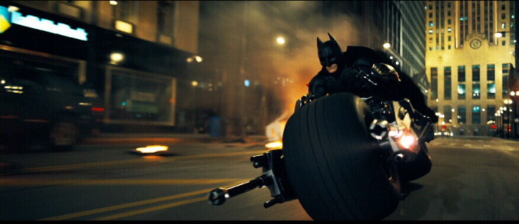 Batman rides through Gotham City on his Bat bike (motorcycle). 