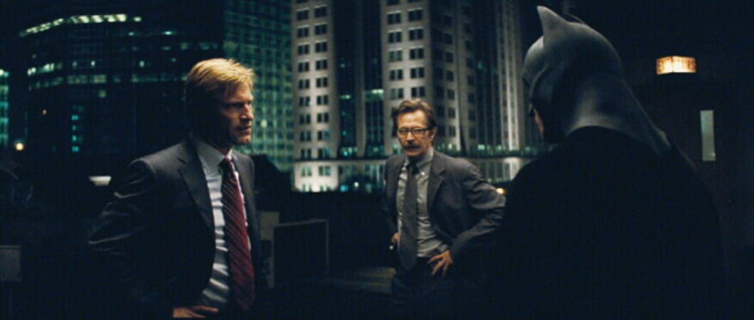 Harvey Dent, Lieutenant James Gordon, and Batman face each other in a circle. 