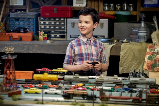 Iain Armitage in a garage with toy train sets and vintage toy cars from the pilot Young Sheldon episode.